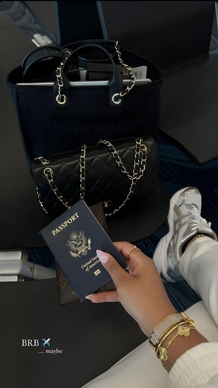 Hand holding a passport with a black handbag and shoes in the background